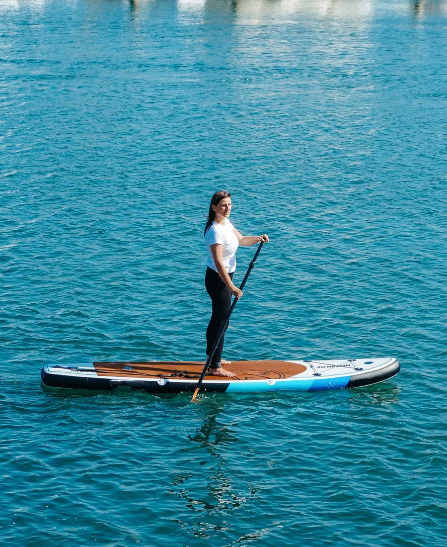 A woman standing on an inflatable paddle board on calm blue water