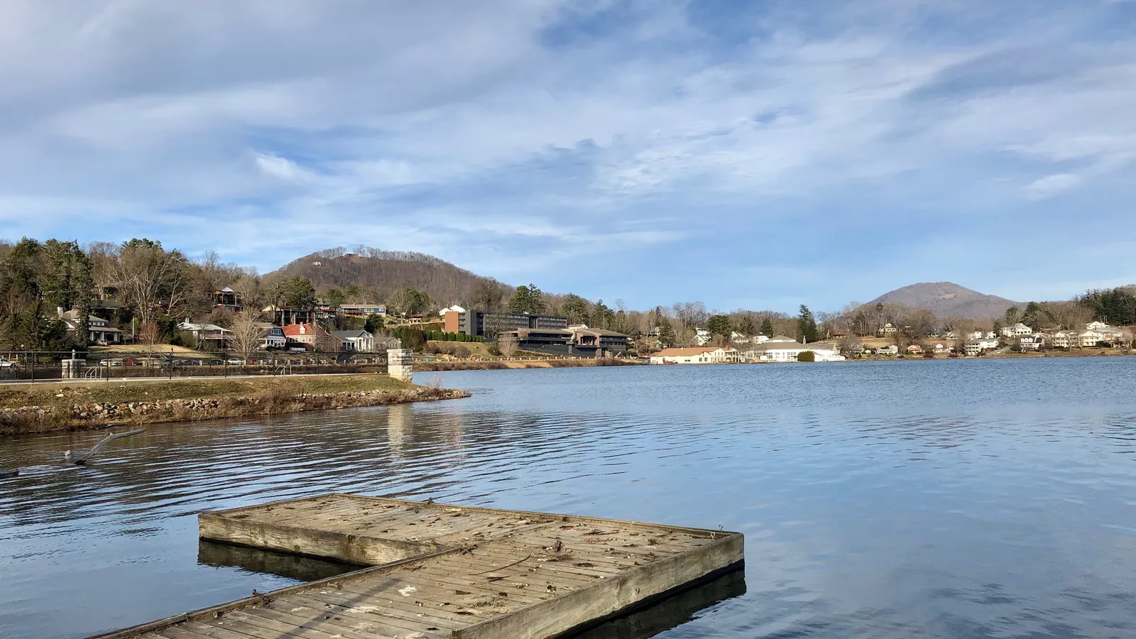 A wooden dock on Lake Junaluska, with lakeside buildings and mountains across the water