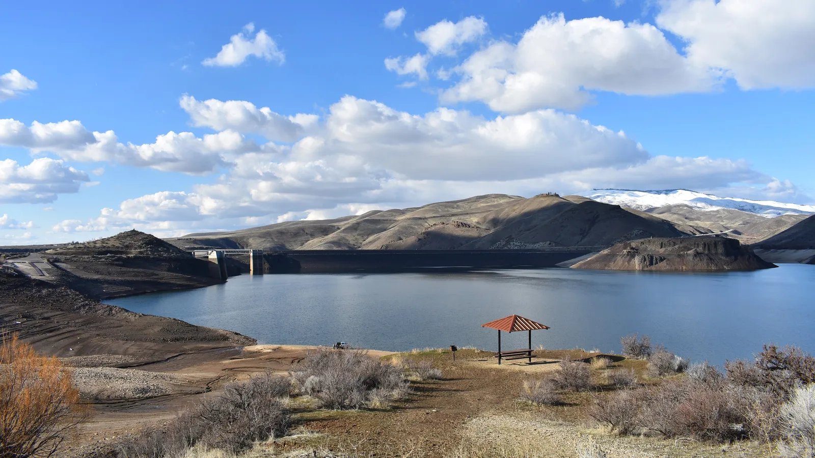 Lucky Peak Lake and Lucky Peak Dam under a cloudy sky, with a picnic shelter in the foreground