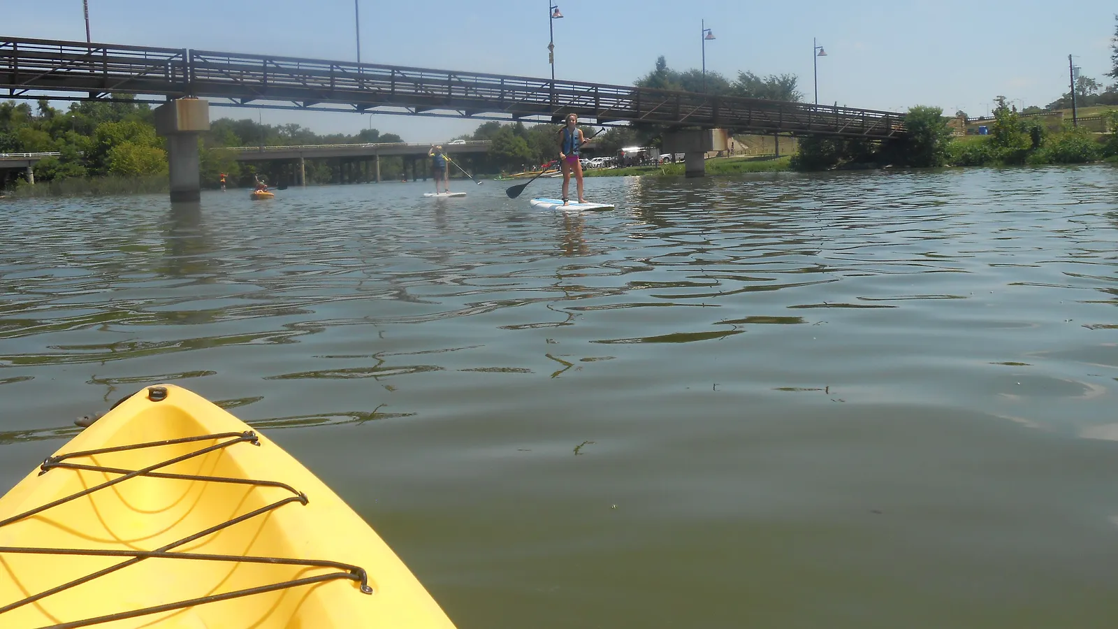 A paddle boarder near the footbridge at the north end of White Rock Lake, seen from a kayak