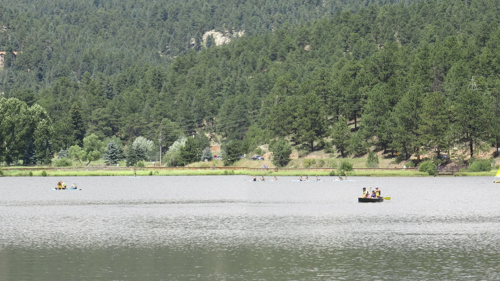 Paddlers and boats on Evergreen Lake below a pine-covered hillside