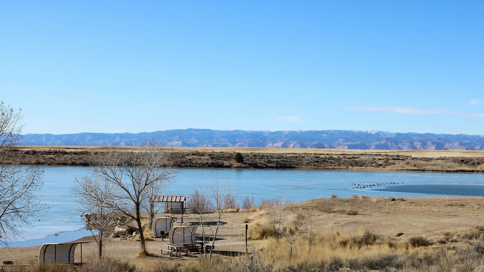 Highline Lake in winter, with picnic shelters on the shore and mountains on the horizon
