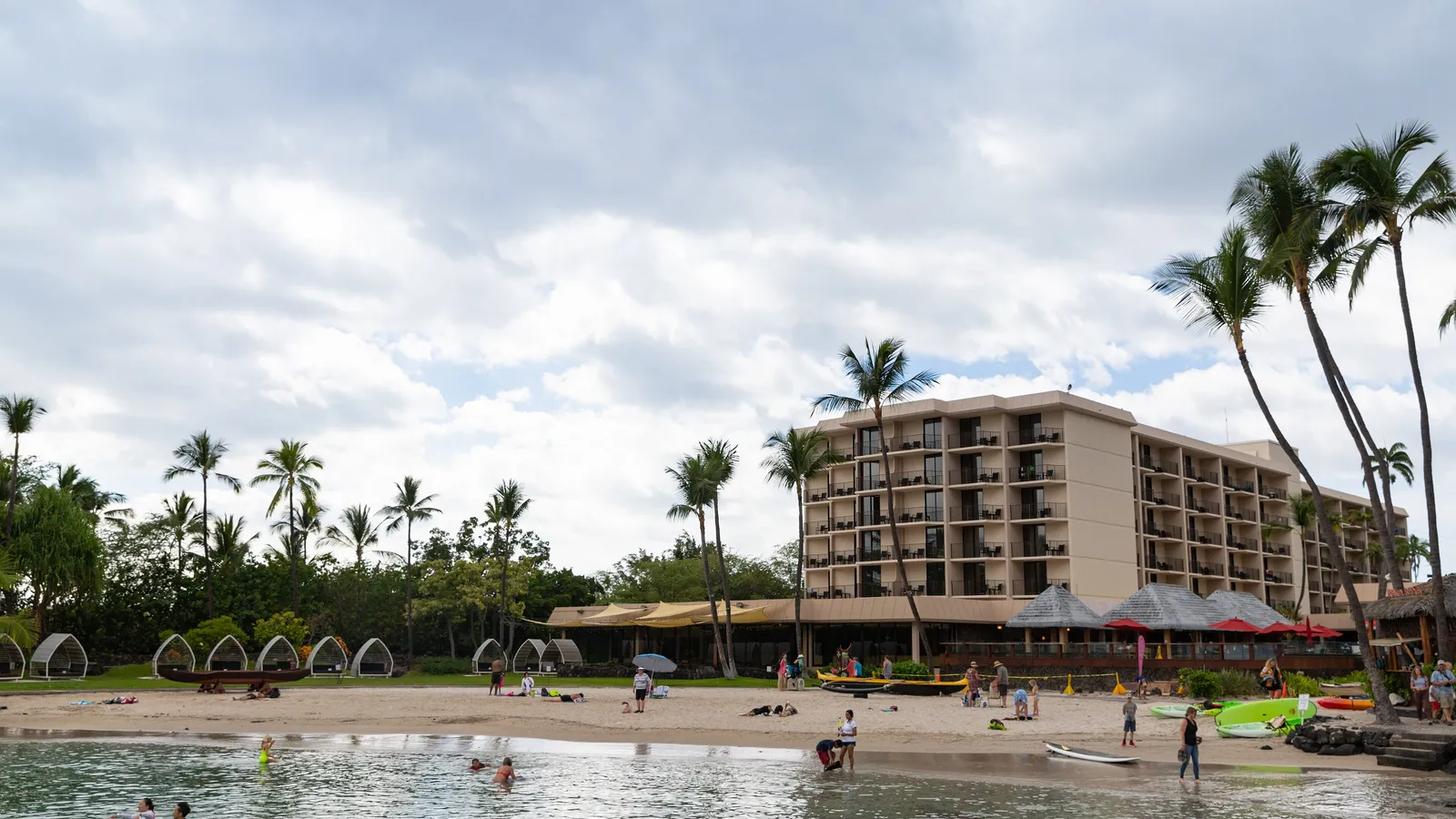 Calm water at Kamakahonu Beach in Kailua-Kona, with palm trees and the hotel behind