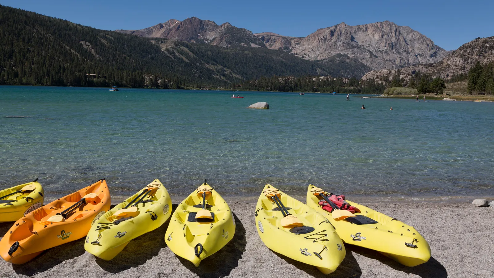 Yellow and orange kayaks on the beach at June Lake, with mountains across the water
