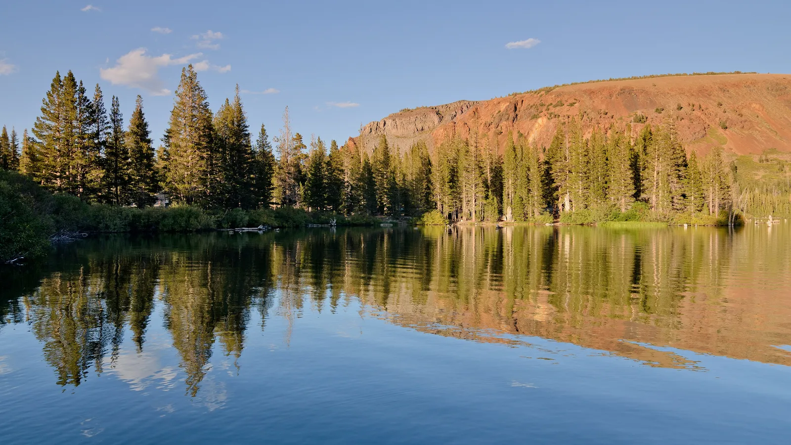 Pines and a red ridge reflected in calm water on Lake Mary at sunset
