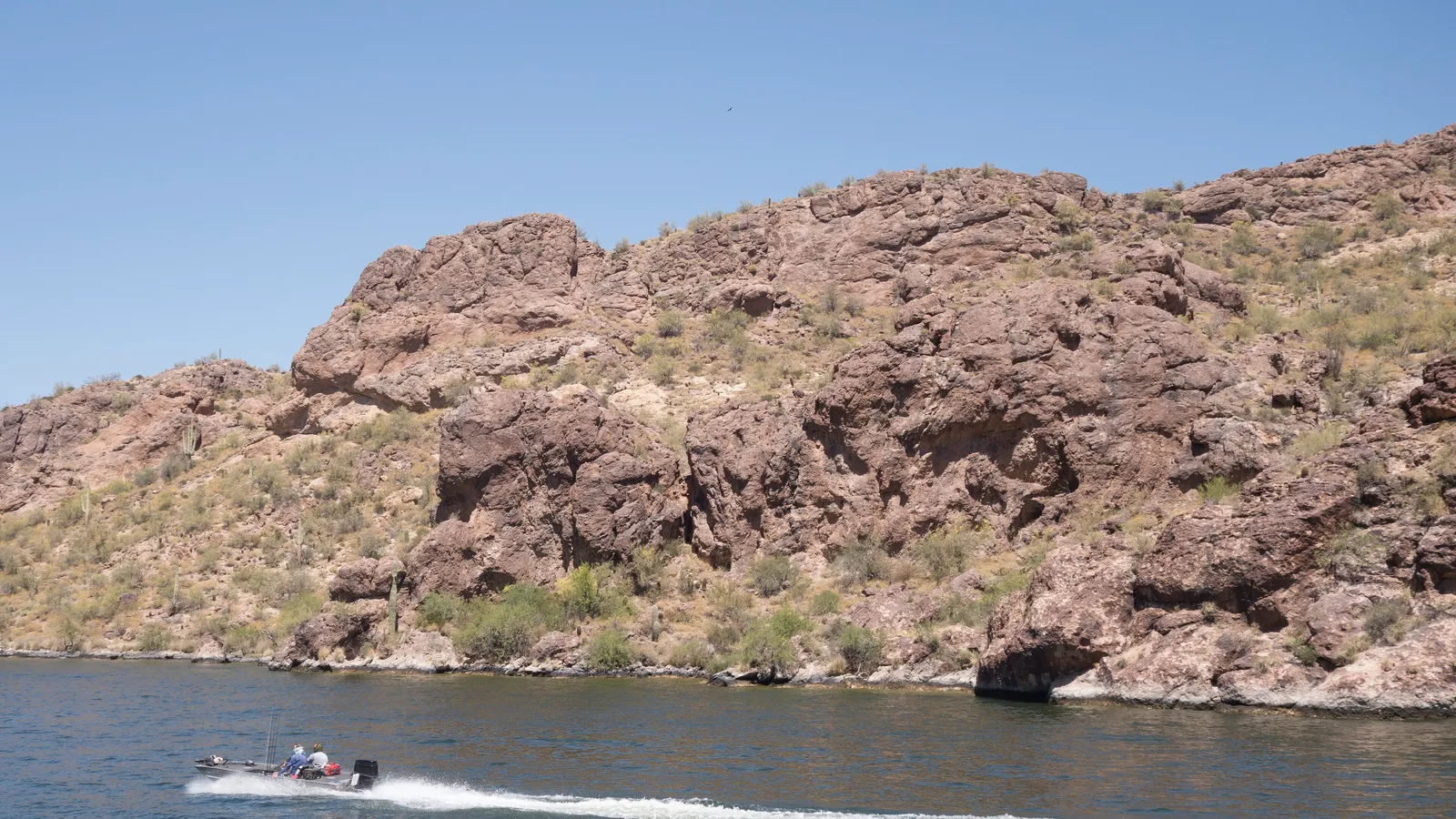 Rocky desert cliffs rising above Saguaro Lake, with a boat passing below