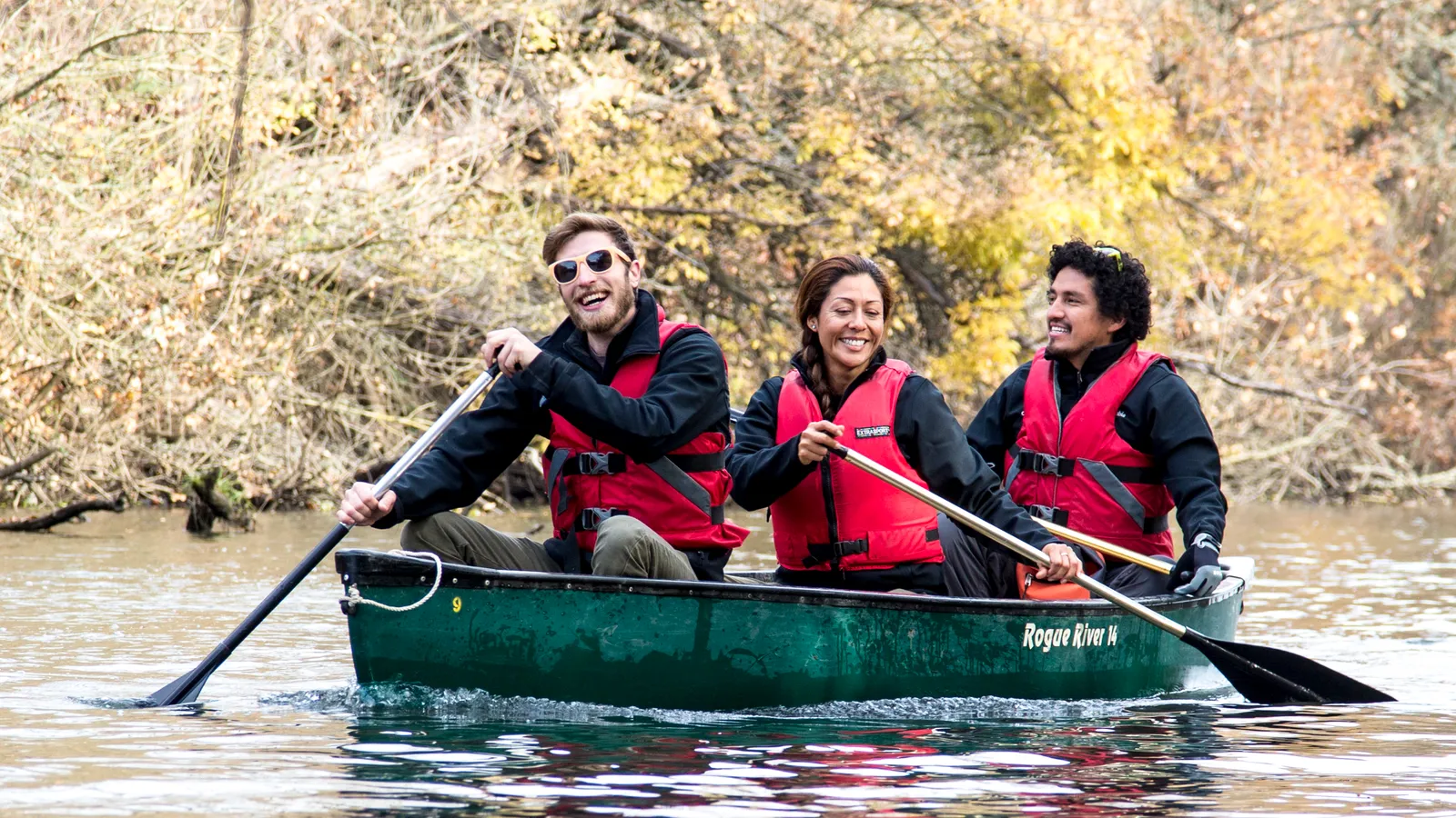 Three people paddling a canoe on the Cosumnes River among bare winter trees