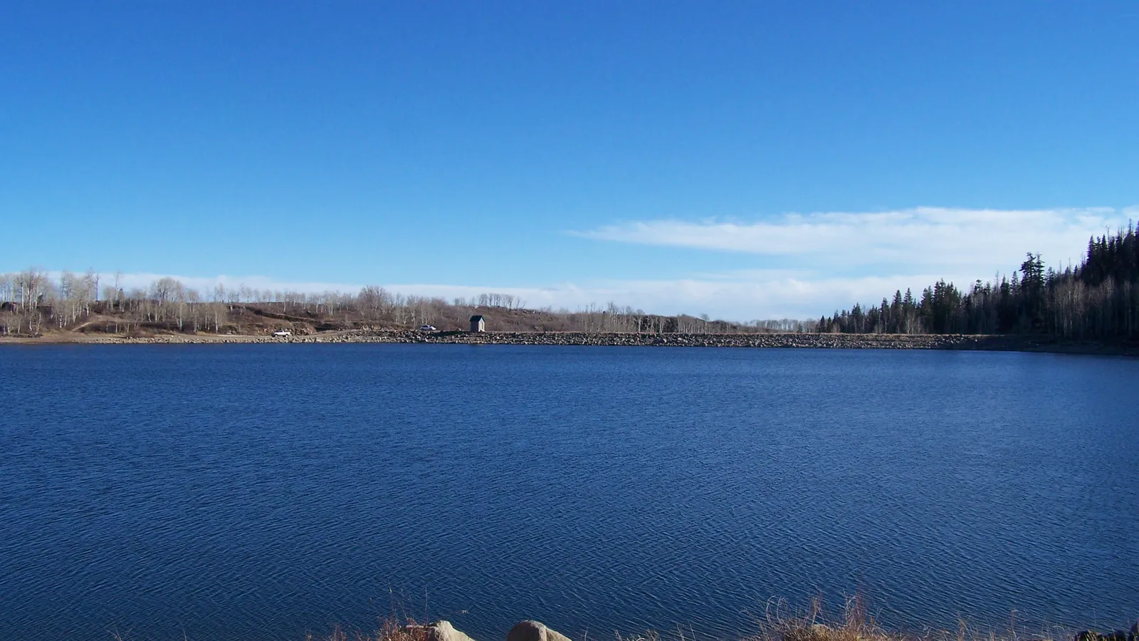 Kolob Reservoir under a blue sky, looking toward the dam, with pines on the far shore