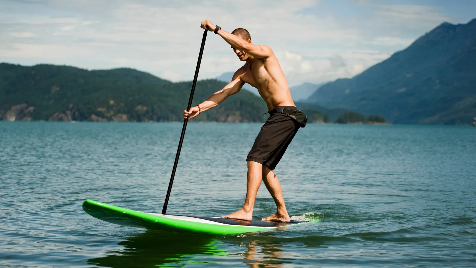 Paddler on a hard board taking a forward stroke on a mountain lake